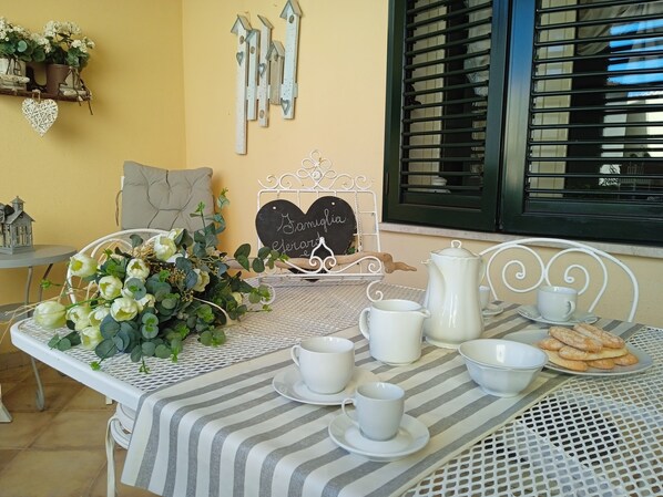 A dining table set with white cups, saucers, a teapot, and pastries, with a heart-shaped sign reading "Samilia & Jerard" and decorative items on the wall.