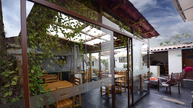 An indoor dining area with wooden tables and chairs, a glass partition with greenery, and a tiled ceiling. - Hotel Boutique Gold Garden (Cusco)