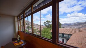 A room with a large window overlooking a town with red-roofed buildings and a mountain range. - Hotel Boutique Gold Garden (Cusco)