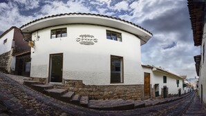 A white building with a curved roof and a sign that reads "GOLD GARDEN." It has a stone base and a cobblestone street in front. - Hotel Boutique Gold Garden (Cusco)