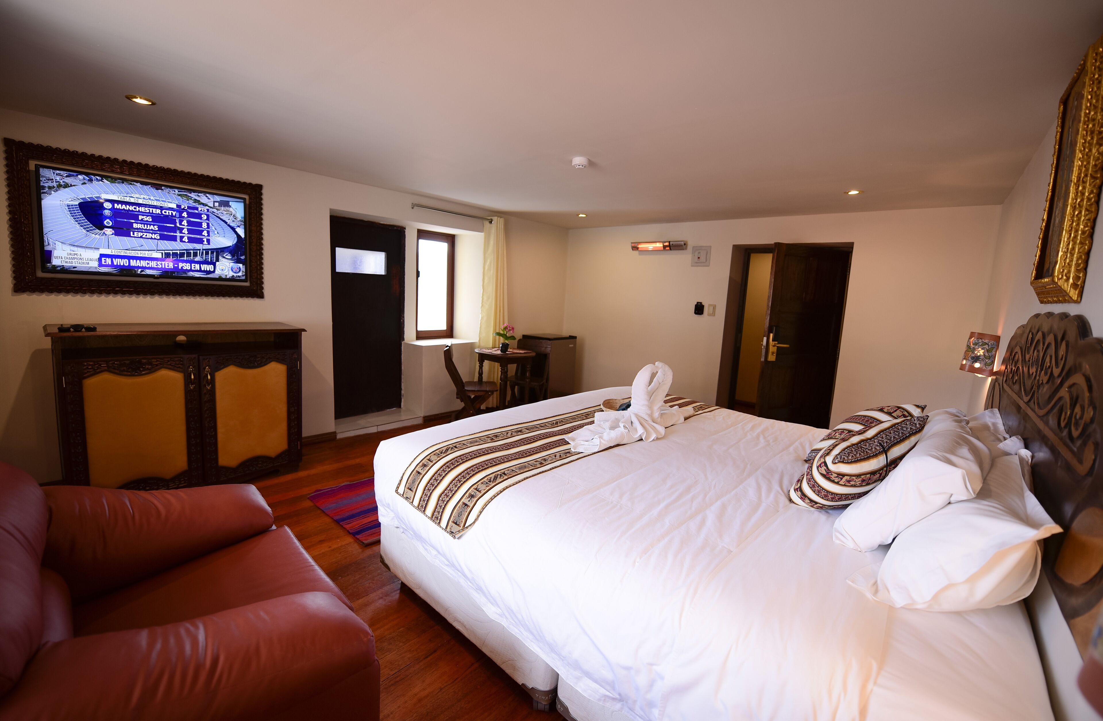 A hotel room with a large bed, a TV mounted on the wall, a desk, and a window.