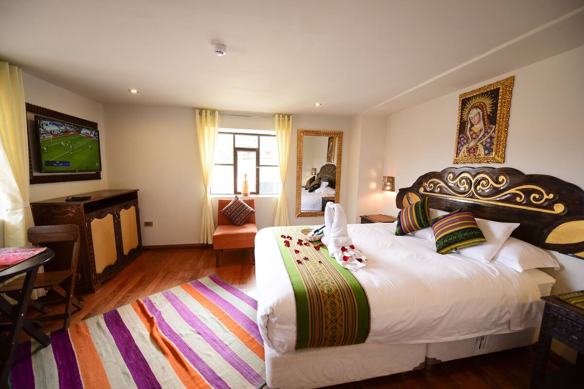 Habitación de hotel con una cama grande, un escritorio, una silla, un televisor y una ventana con cortinas.