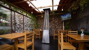 An outdoor dining area with wooden tables and chairs, a stone wall, and a television screen. - Hotel Boutique Gold Garden (Cusco)