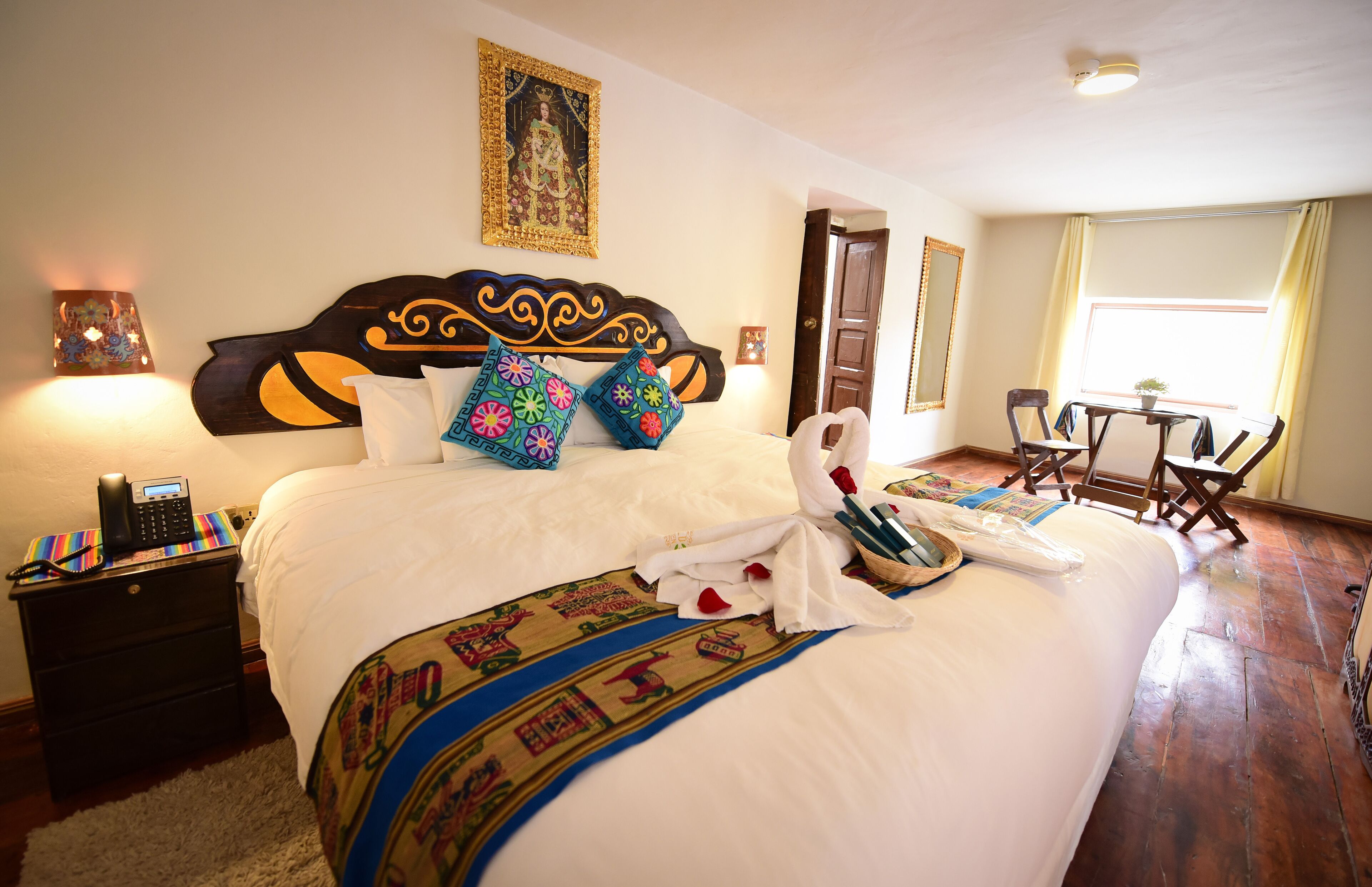 A hotel room with a large bed, a bedside table with a phone, a wall-mounted lamp, and a window with curtains.