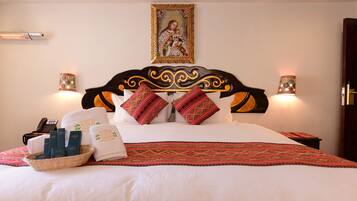 A neatly made bed with a patterned bedspread, two decorative pillows, a framed religious painting above the bed, and two wall-mounted lamps.
