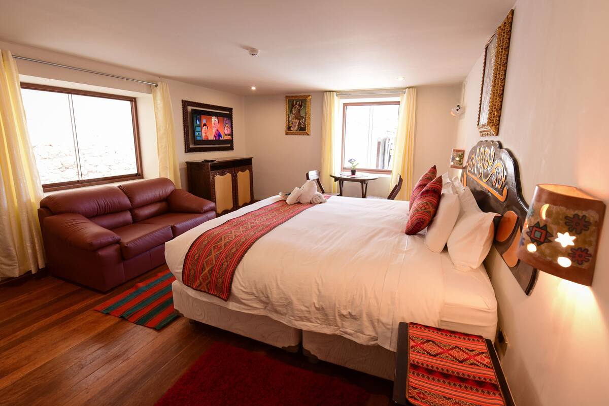 Una habitación de hotel con una cama grande, un sofá, un televisor y una mesita.