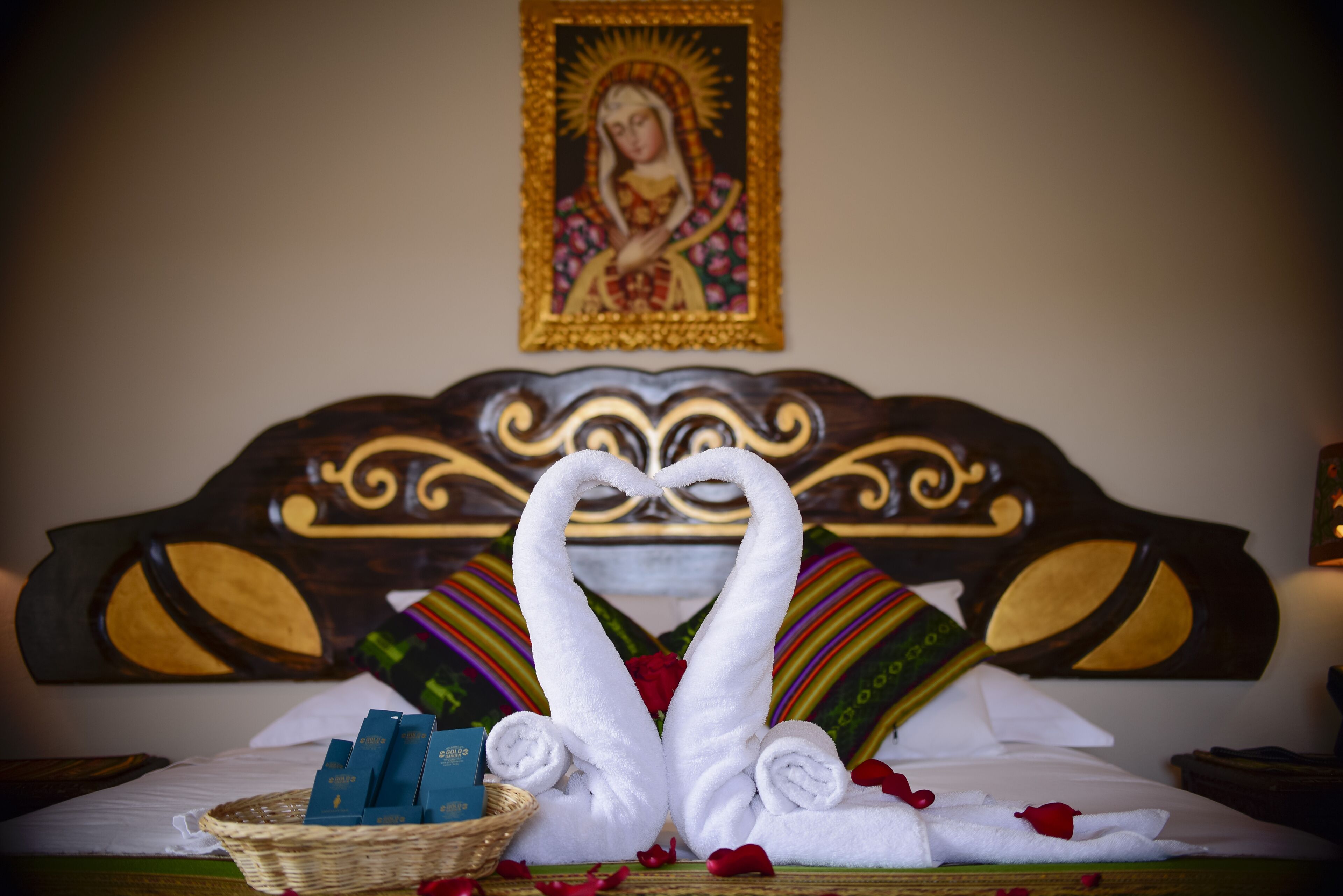 Una cama con un cabecero decorativo, un cuadro religioso enmarcado y una cesta con artículos de aseo.