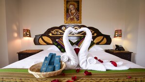 A neatly made bed with a decorative towel arrangement, a basket of toiletries, and a religious painting on the wall. - Hotel Boutique Gold Garden (Cusco)