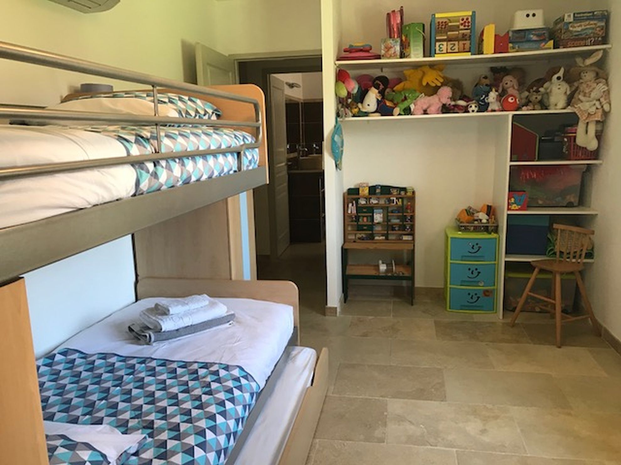A bunk bed room with a desk and shelves filled with toys and books.