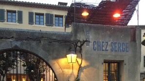 A restaurant named "Chez Serge" with an outdoor seating area, a large potted plant, and a signboard. - Pool, 4 chambres, 4 SdB, clima, cuisine extérieure, grands jardins, aire de jeux (Carpentras)
