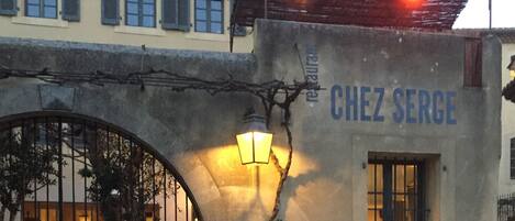 Un restaurante llamado "Chez Serge" con terraza, una planta grande en maceta y un cartel.