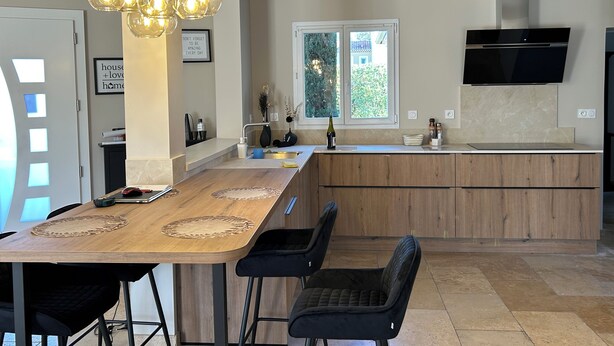 A modern kitchen with a wooden island, pendant lighting, a built-in TV, and a window with a view of greenery. - Pool, 4 chambres, 4 SdB, clima, cuisine extérieure, grands jardins, aire de jeux (Carpentras)