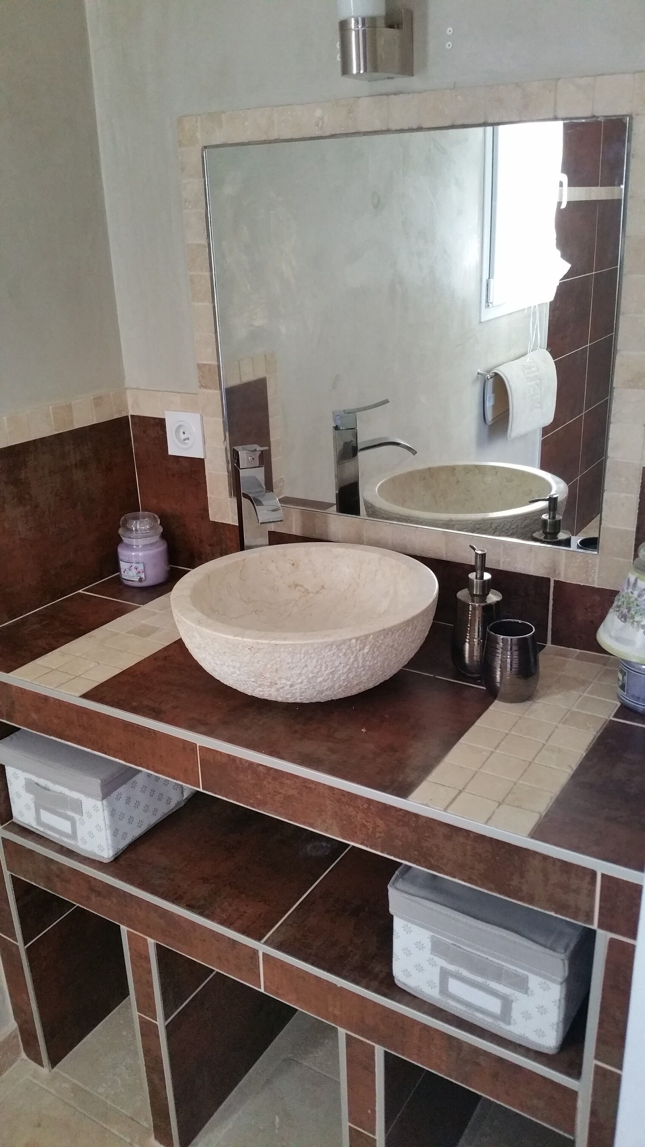 A bathroom with a large round sink, a mirror, and a towel rack. There are storage drawers below the sink.