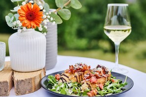 Una mesa de comedor con un plato de comida, una copa de vino blanco y un florero con flores.
