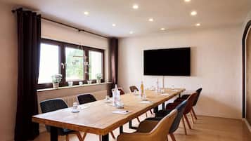 Una sala de conferencias con una larga mesa, sillas, un televisor de pantalla plana y ventanas con cortinas.