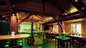 A rustic wooden interior with high ceilings and exposed beams, featuring multiple seating areas with green cushioned chairs and wooden tables. - Landhotel Grashof (Kalbach)