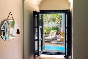 An open door leading to a pool area with lounge chairs and a potted plant.