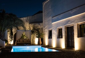 A nighttime pool area with a clear pool, a covered seating area, and a building with a dark door and windows.