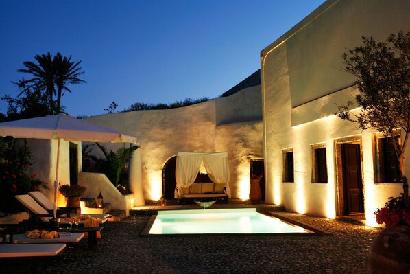 A pool area with a canopy, lounge chairs, and a bed with a canopy.
