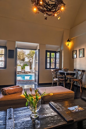 A room with a dining table, chairs, a vase with flowers, a bench, and a view of an outdoor swimming pool.