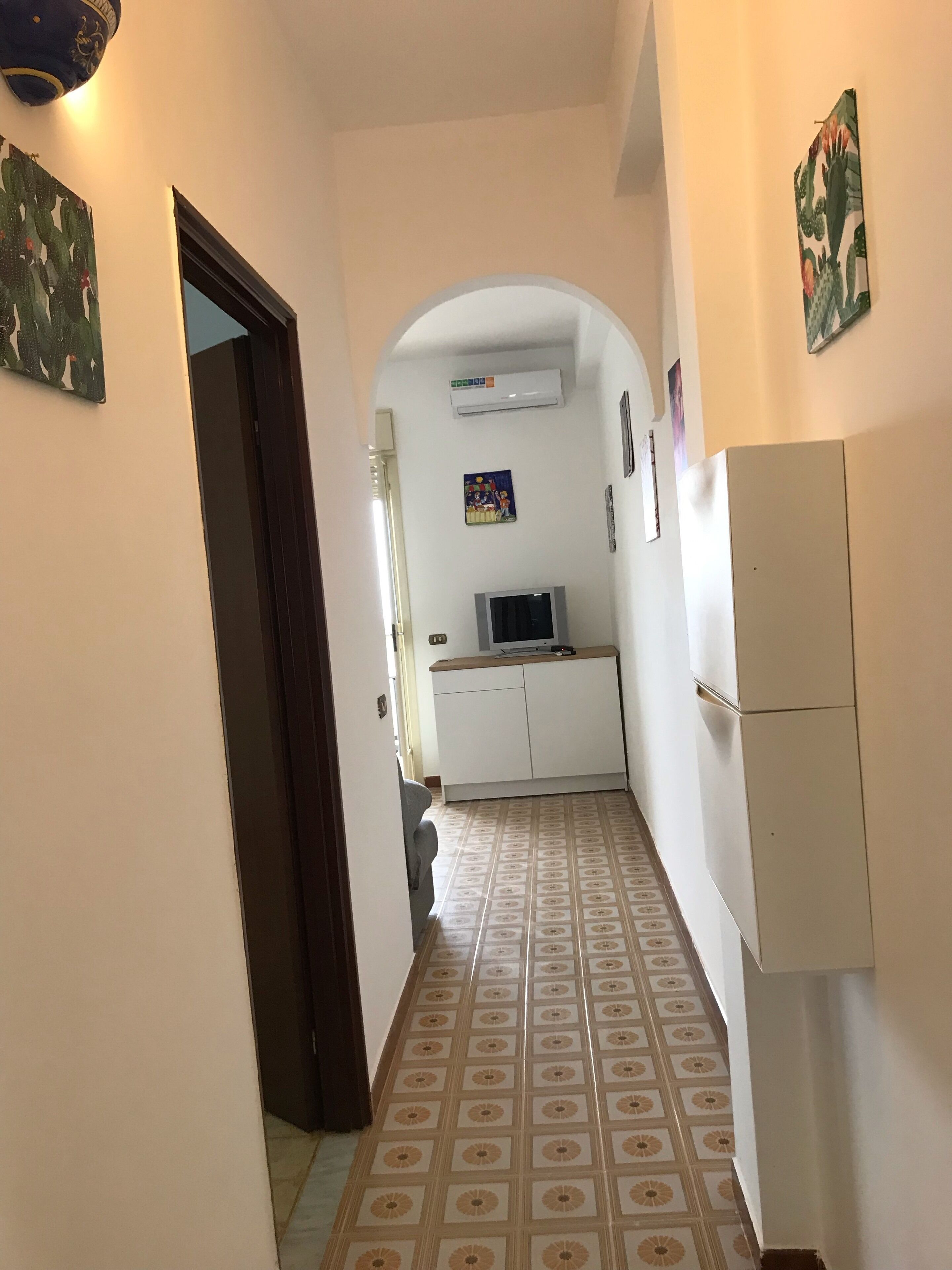 Un couloir étroit avec des carreaux de sol à motifs, un réfrigérateur blanc et un téléviseur posé sur un meuble.