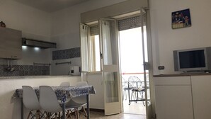 A compact kitchen with a dining area, a TV, and a balcony with a view.