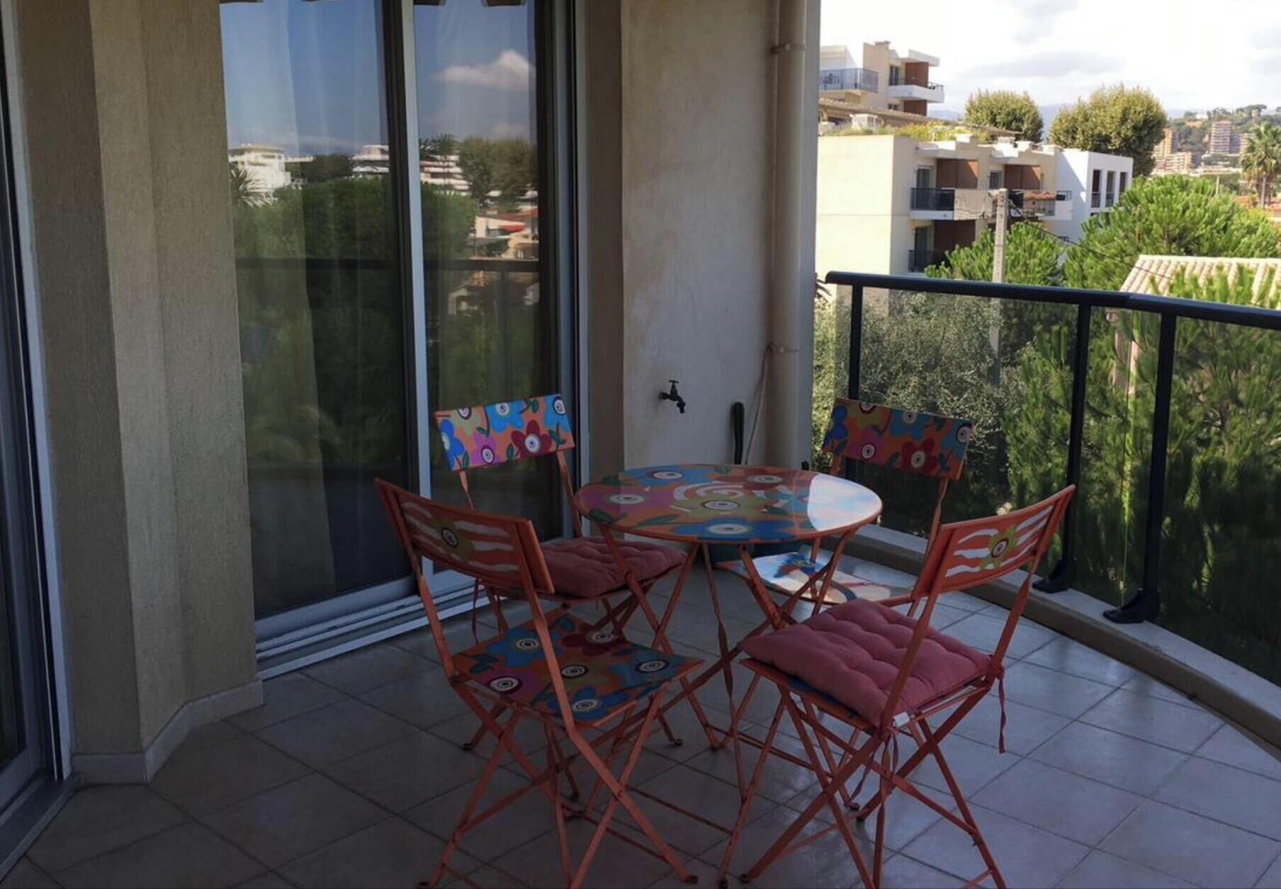 A balcony with a table and chairs, a sliding glass door, and a view of the surrounding neighborhood.