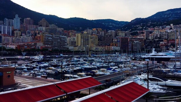 Una marina piena di barche, uno skyline con diversi edifici e montagne sullo sfondo.