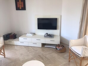 A modern living room with a flat-screen TV mounted on a white cabinet, a laptop on a stand, and a wicker basket on the floor.