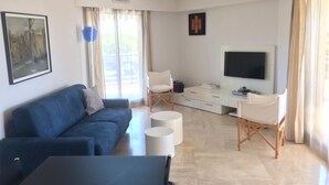 Un soggiorno moderno con un divano blu, una TV a schermo piatto, un tavolino da caffè e un'area pranzo con una sedia bianca e un piccolo tavolo.