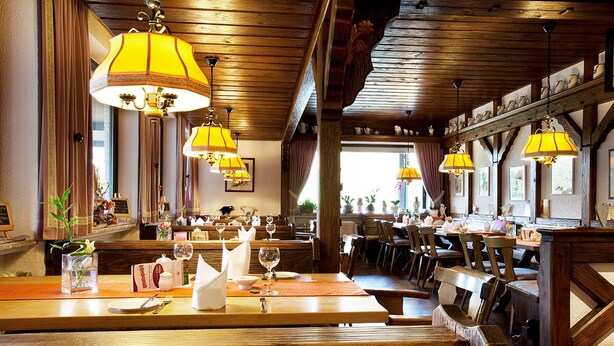 A restaurant with wooden beams, yellow lamps, and neatly arranged tables and chairs. - Flörsbacher Hof (Floersbachtal)