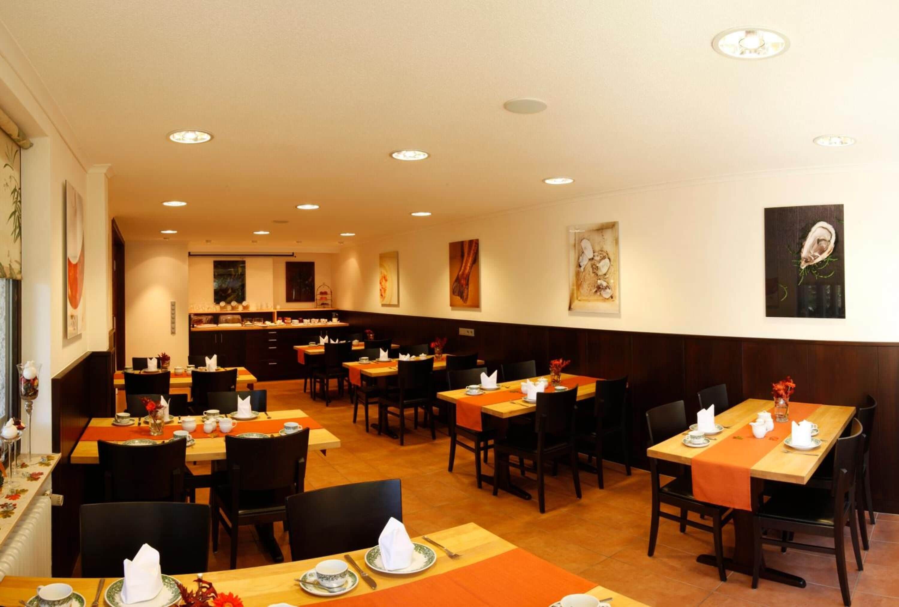Un restaurante con varias mesas y sillas, una cocina al fondo y obras de arte en las paredes.