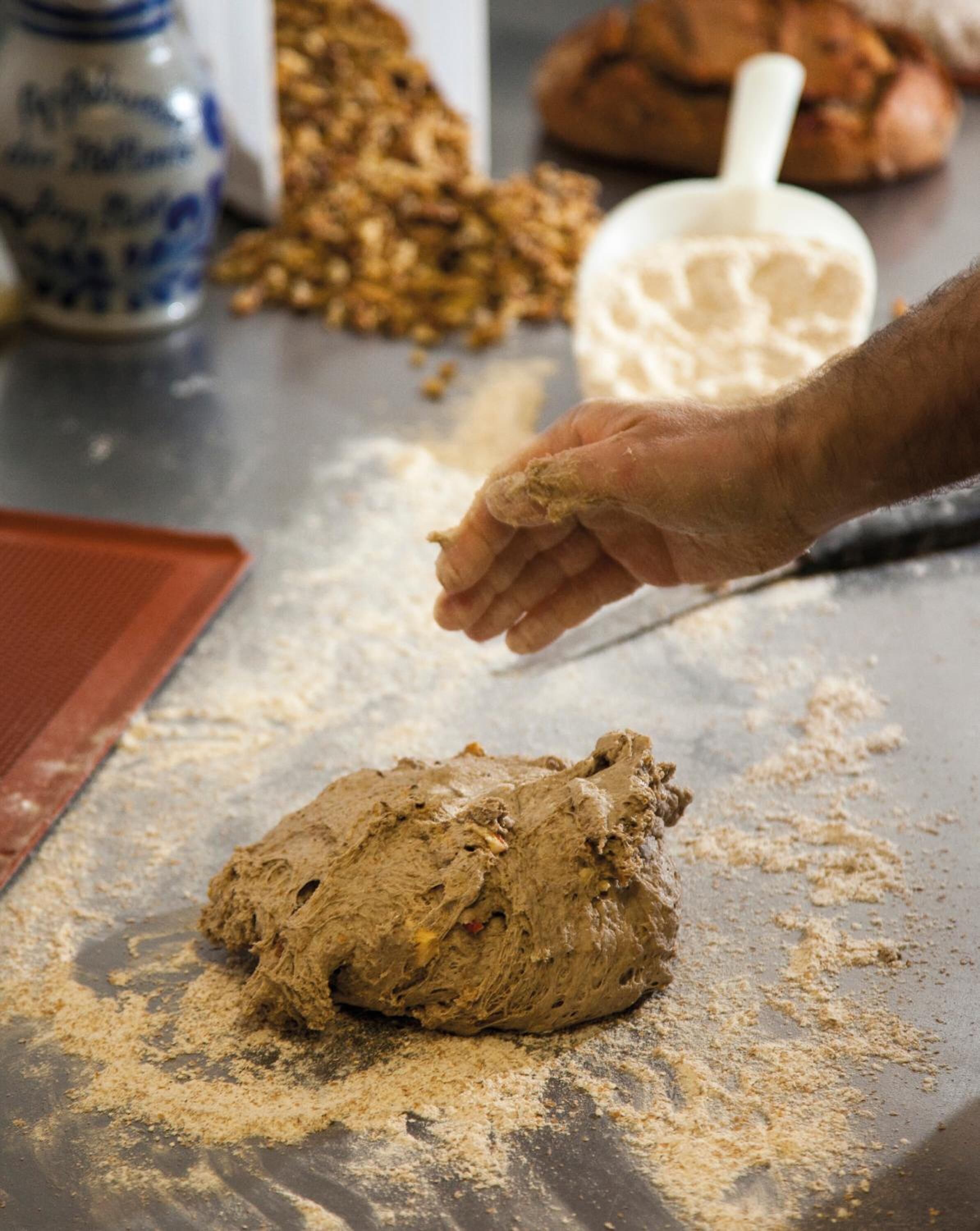 Une personne pétrit de la pâte sur une surface farinée, à l'aide d'un rouleau à pâtisserie, et un pot de farine se trouve à proximité.