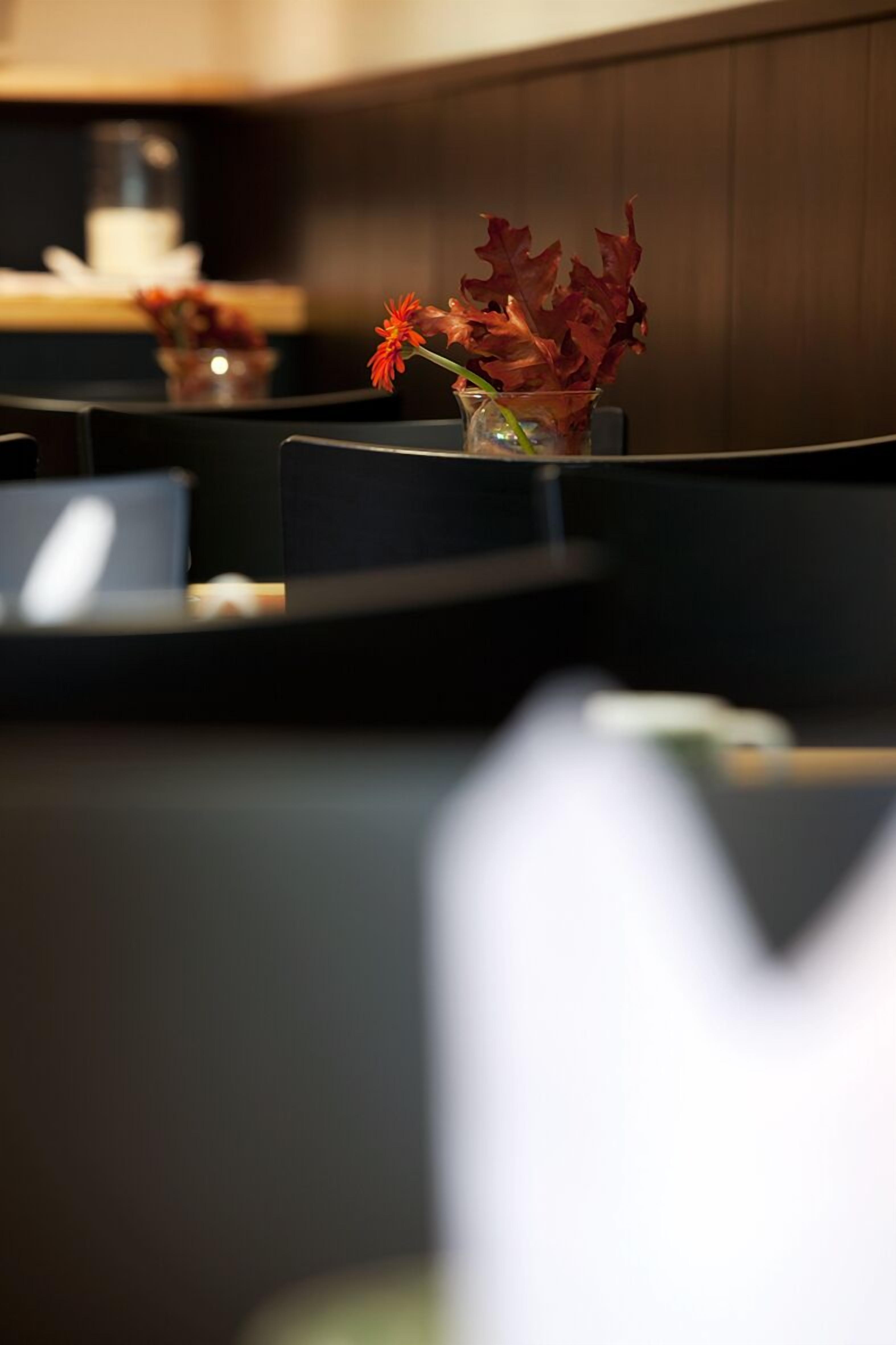 A restaurant setting with a table, chairs, and a vase with red flowers.