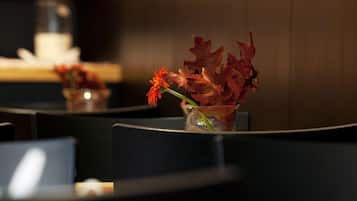 A restaurant setting with a table, chairs, and a vase with red flowers.
