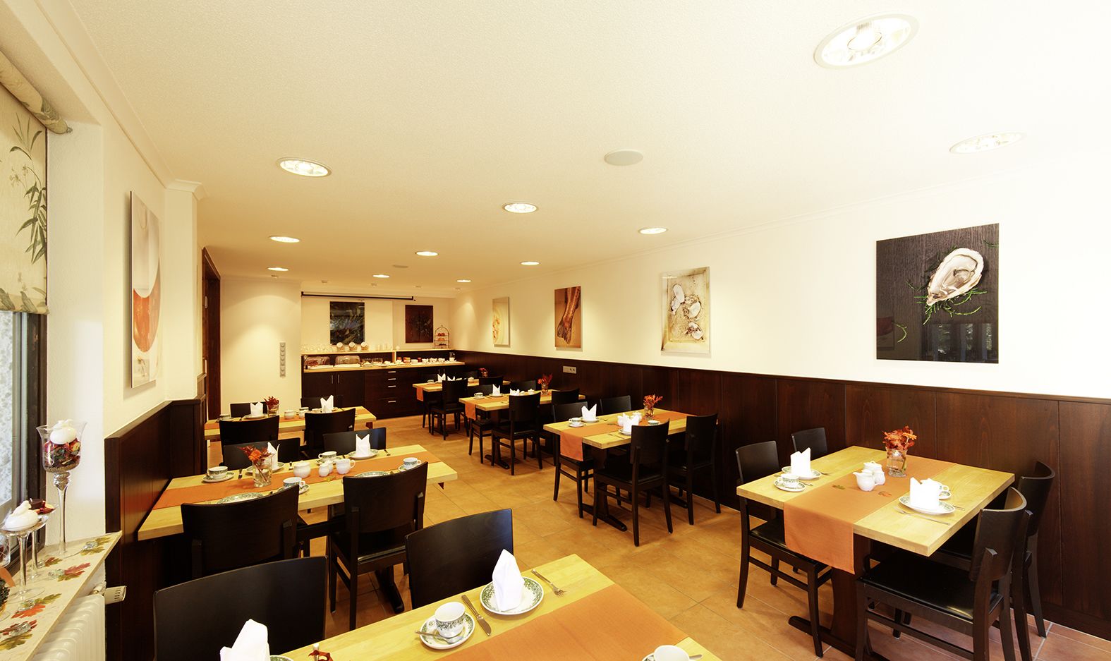 A restaurant with multiple tables and chairs, wooden paneling on the walls, and ceiling lights.