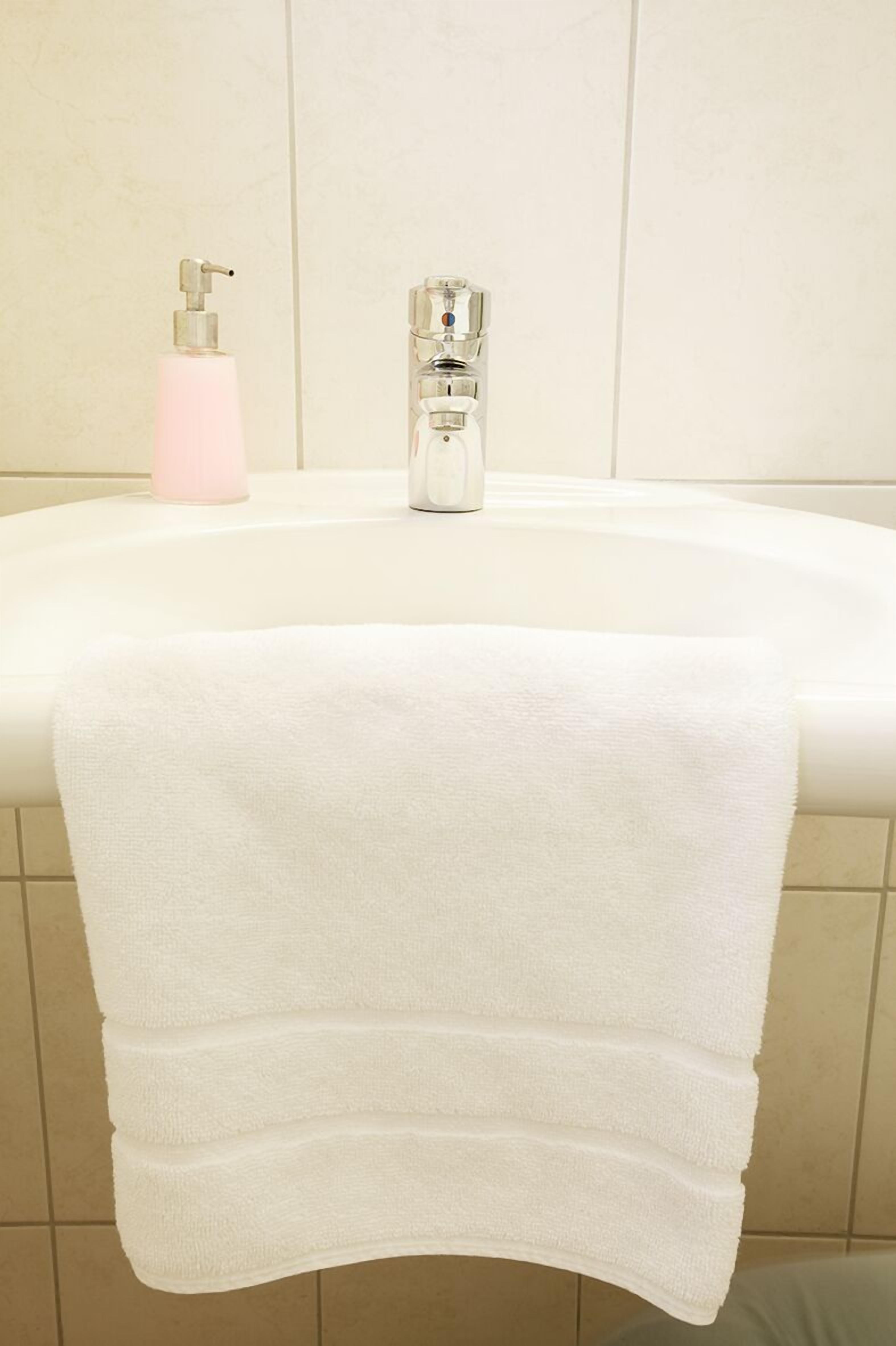 Un baño con una bañera blanca, un dispensador de jabón rosa y un grifo cromado.