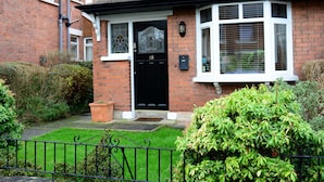 A brick house with a black front door, a small garden, and a black metal fence.