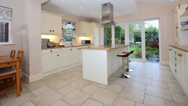 A spacious kitchen with a central island, white cabinetry, and a large window providing a view of the garden.