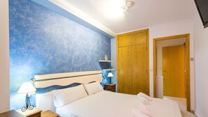 A bedroom with a bed, bedside table, lamp, and wooden wardrobe. - ApartUP Saplaya Harbour (Alboraya)