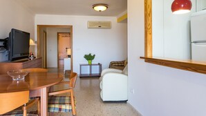 A compact living space with a dining area, a white sofa, a television, and a red pendant light. - ApartUP Saplaya Harbour (Alboraya)