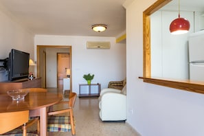 A compact living space with a dining area, a white sofa, a television, and a red pendant light. - ApartUP Saplaya Harbour (Alboraya)