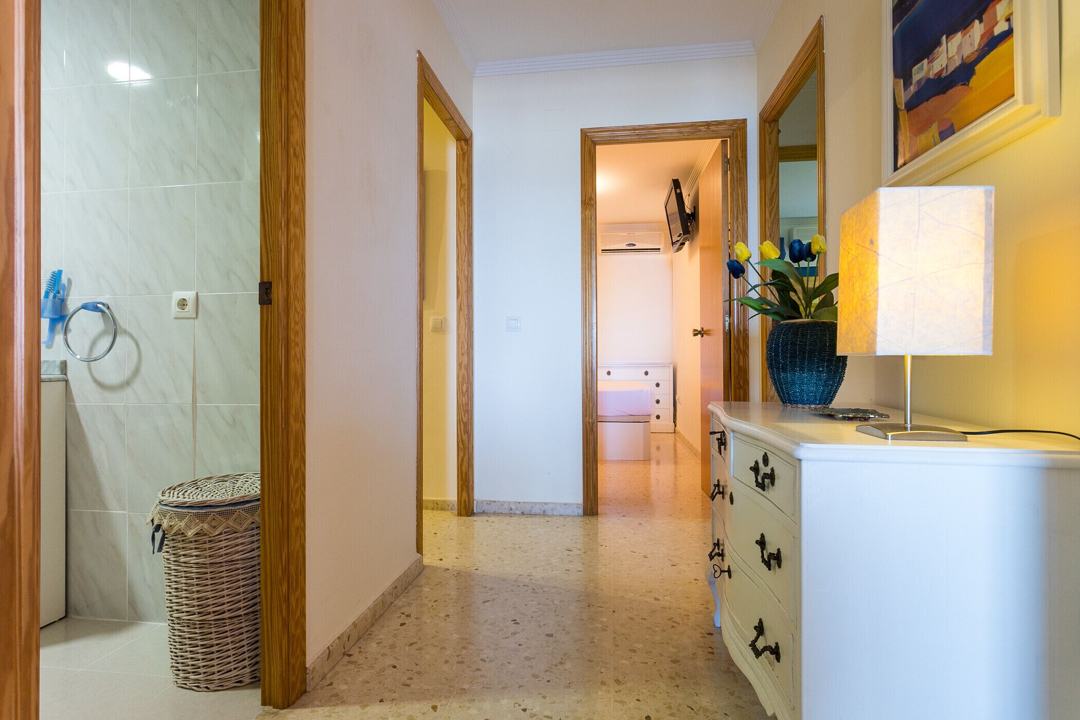 A hallway with a tiled wall, a wicker basket, a white cabinet with drawers, and a mirror on the wall.