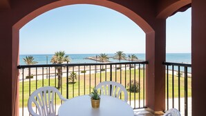 A balcony with a white table and chairs, overlooking a beach with palm trees and a clear sky. - ApartUP Saplaya Harbour (Alboraya)
