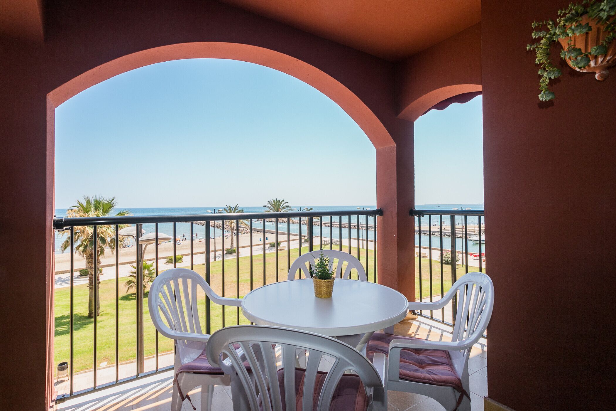 A balcony with a white table and chairs, overlooking a beach and the sea.