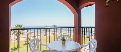A balcony with a white table and chairs, overlooking a beach and the sea.