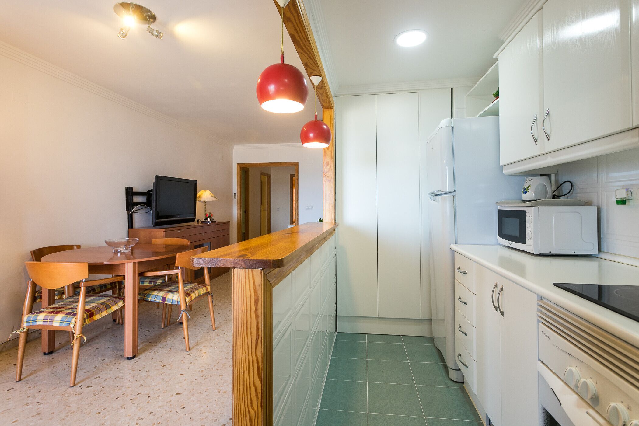 A compact kitchen with white cabinets, a microwave, a stove, and a dining area with a wooden table and chairs.
