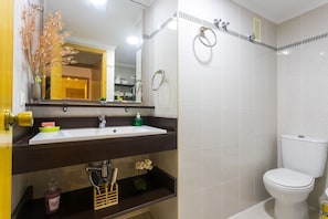 A bathroom with a white sink, mirror, and toilet. There are shelves with toiletries and a decorative plant.