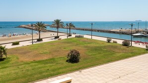 A coastal promenade with a grassy area, palm trees, and a view of the sea. - ApartUP Saplaya Harbour (Alboraya)