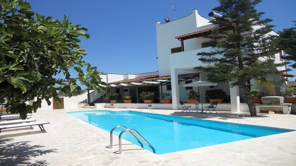 A modern pool area with a clear blue pool, surrounded by white walls and potted plants.